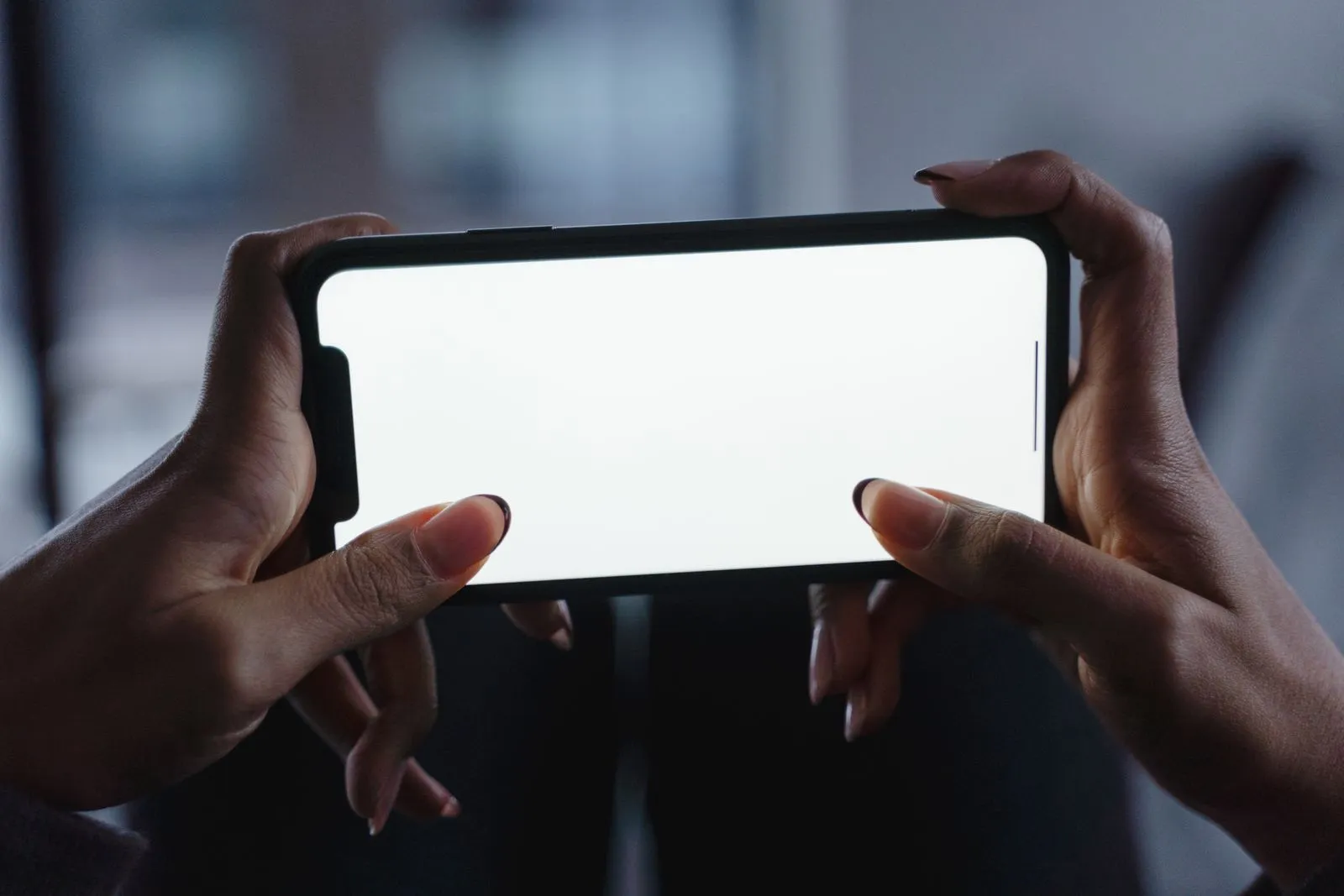 画面に何も表示されていないスマートフォンを両手で持つ手元