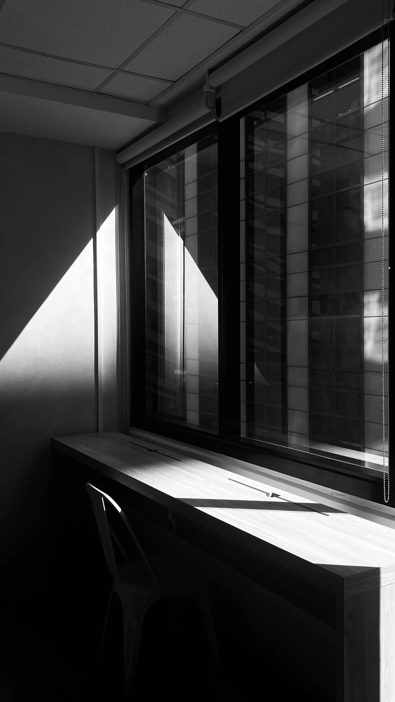 窓辺に日差しと影が落ちた室内をモノクロで写したもの