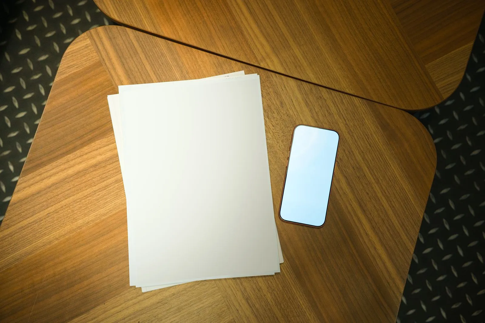 木のテーブルに広げた白紙とスマートフォンを上から見たところ