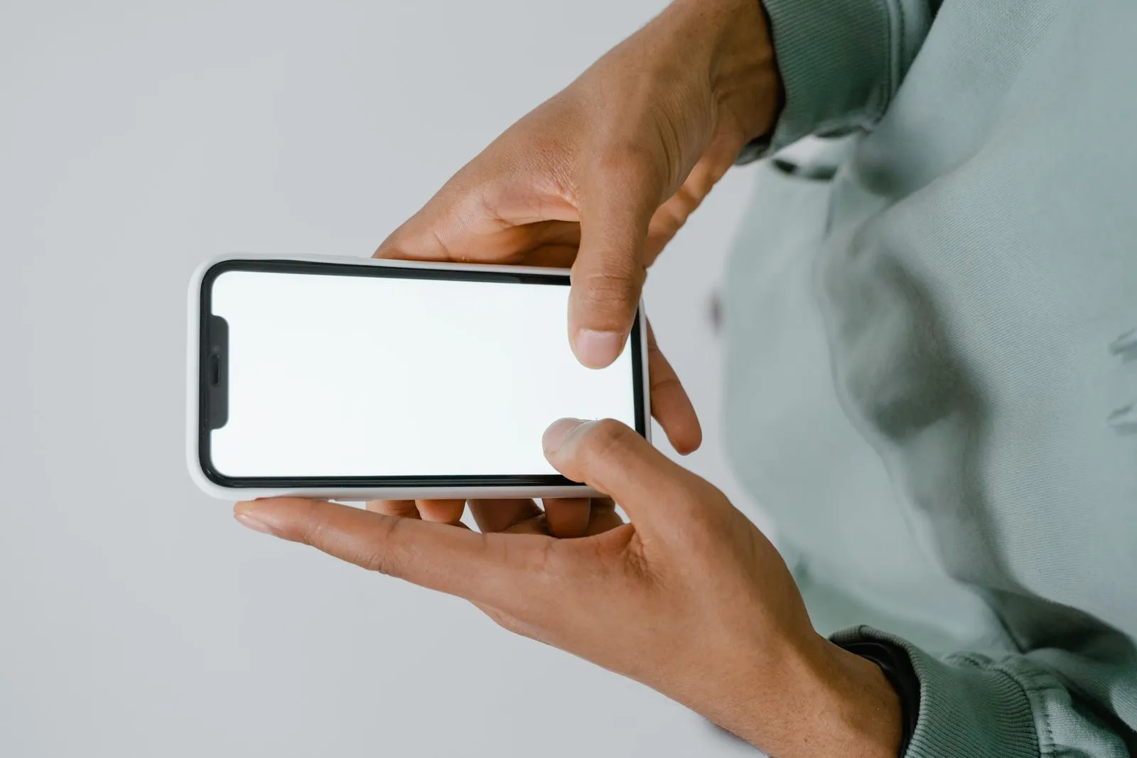 画面に何も表示されていないスマートフォンを片手で持つ手元