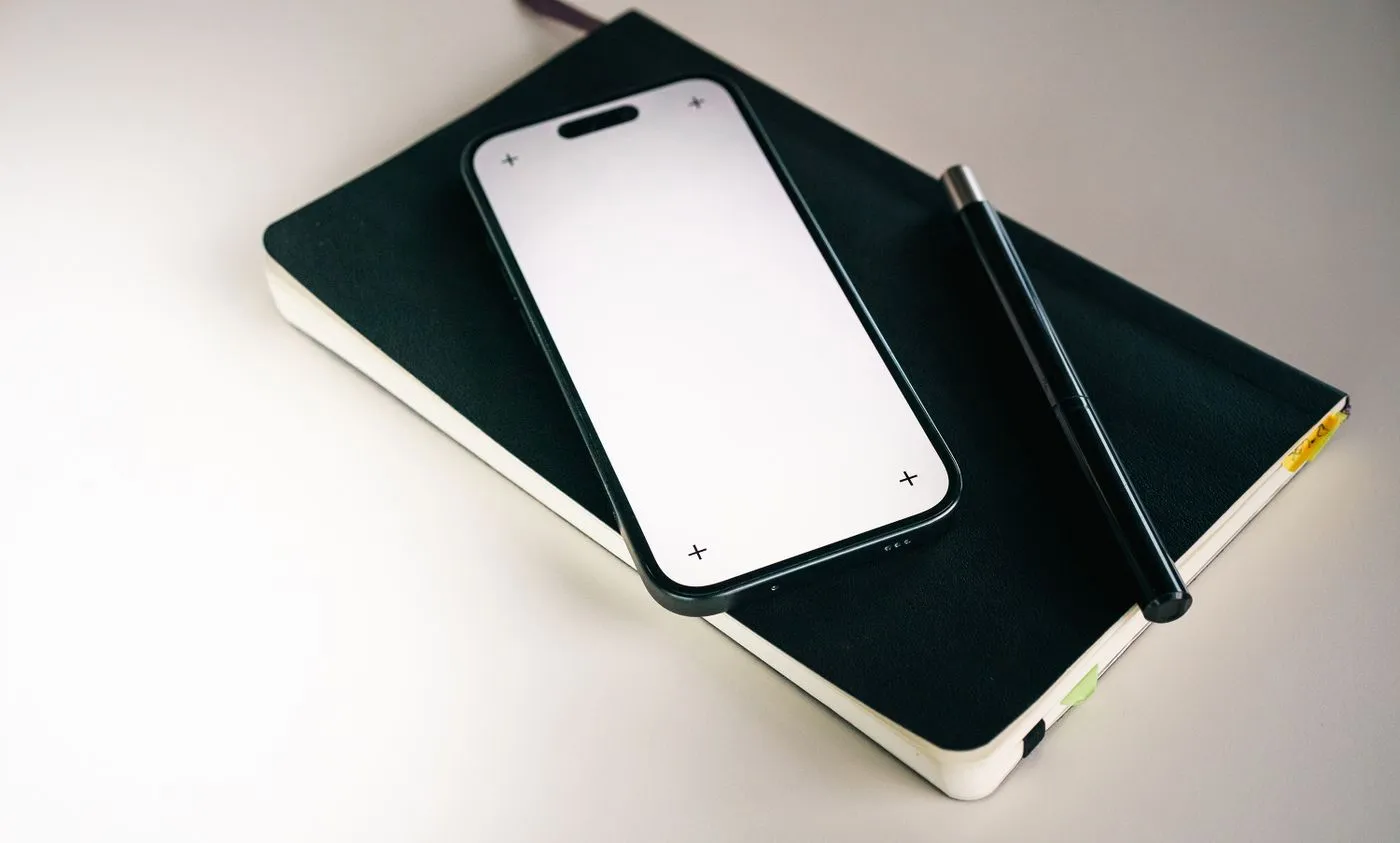 黒い表紙のノートの上に置かれたスマートフォンとペン